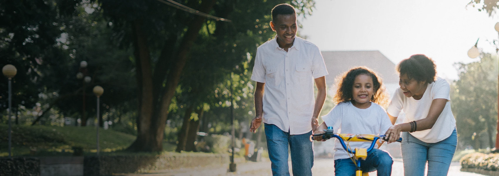 Parents helping child learn to ride a bike.